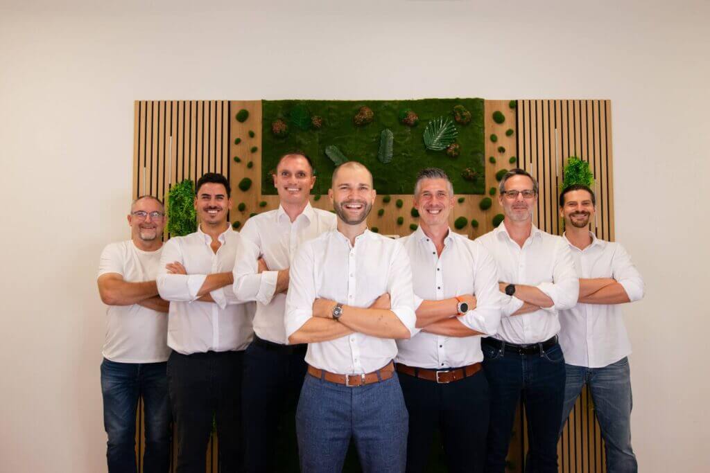 Eine Gruppe von Männern in weißen Hemden posiert vor einer grünen Wand. Teamwork und Professionalität.