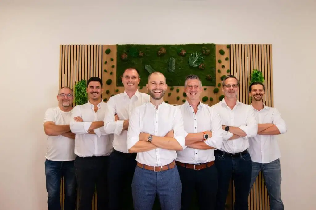 Eine Gruppe von Männern in weißen Hemden posiert vor einer grünen Wand. Teamwork und Professionalität.